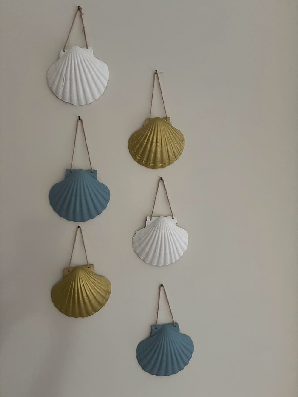 Six coquillages peints en blanc, bleu et jaune, suspendus au mur