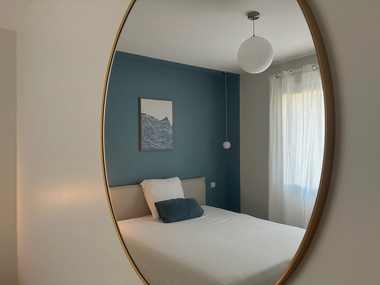 Le miroir rond reflétant le lit et la gravure de vague