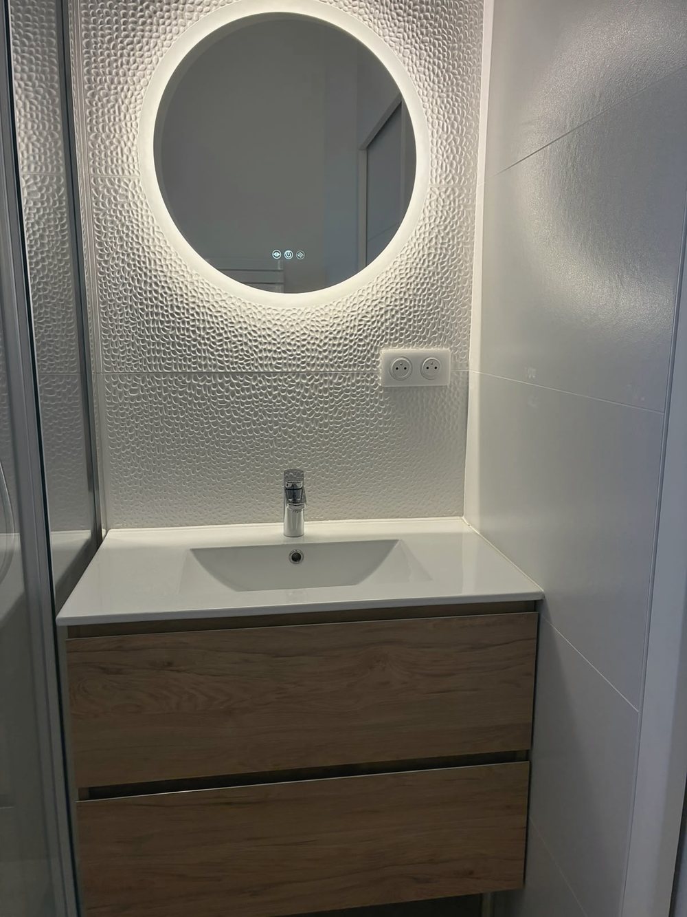 La vasque de la salle d’eau sous le miroir rond rétroéclairé