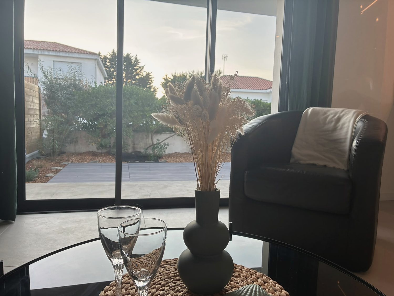 Deux verres sur la table basse, baie vitrée et jardin au couchant